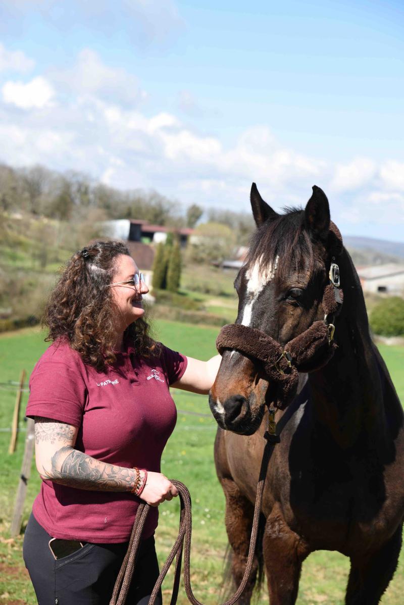 Margaux, gérante des écuries de Malebarthe, tenant un cheval bai dans un champs